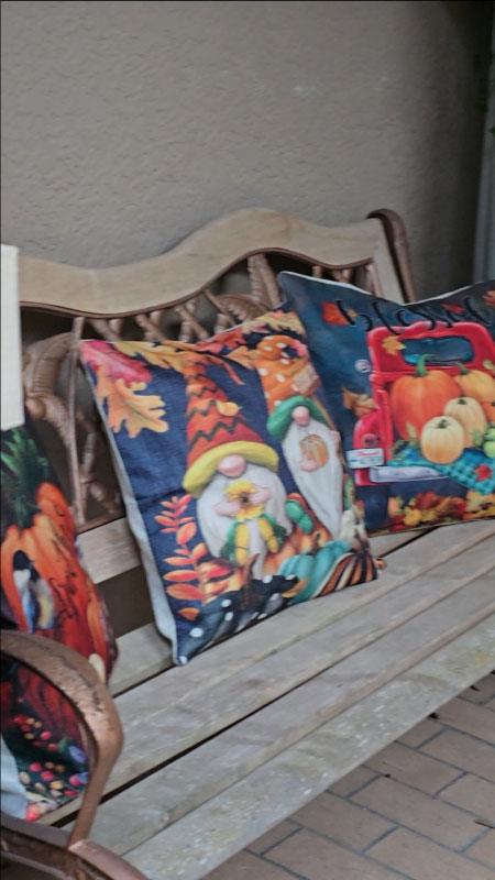Wooden bench with three colorful fall pillows featuring pumpkins and autumn patterns