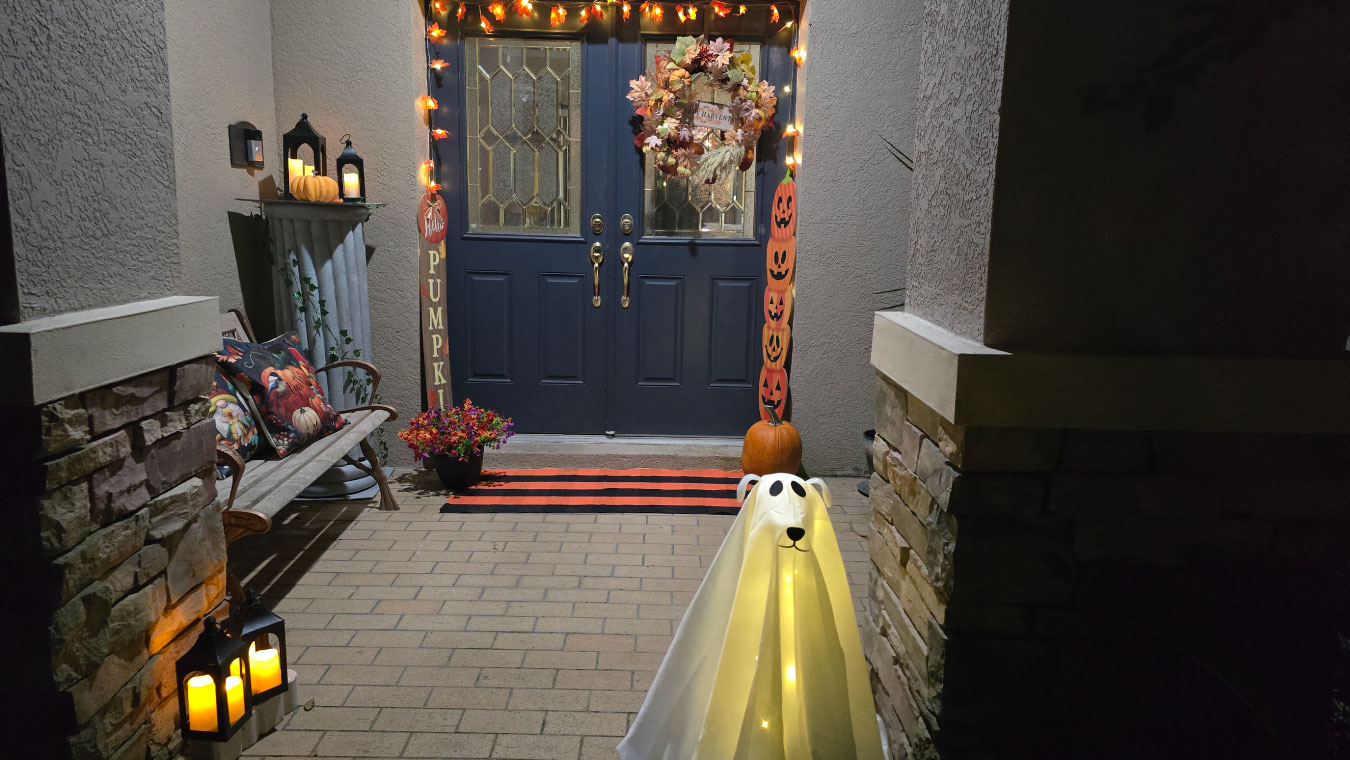 1. Full Porch Photo: Fall front porch decorated with a glowing ghost dog, plaid rug, pumpkin signs, lanterns with LED candles, a fall wreath, maple leaf lights, and a bench with colorful fall pillows.