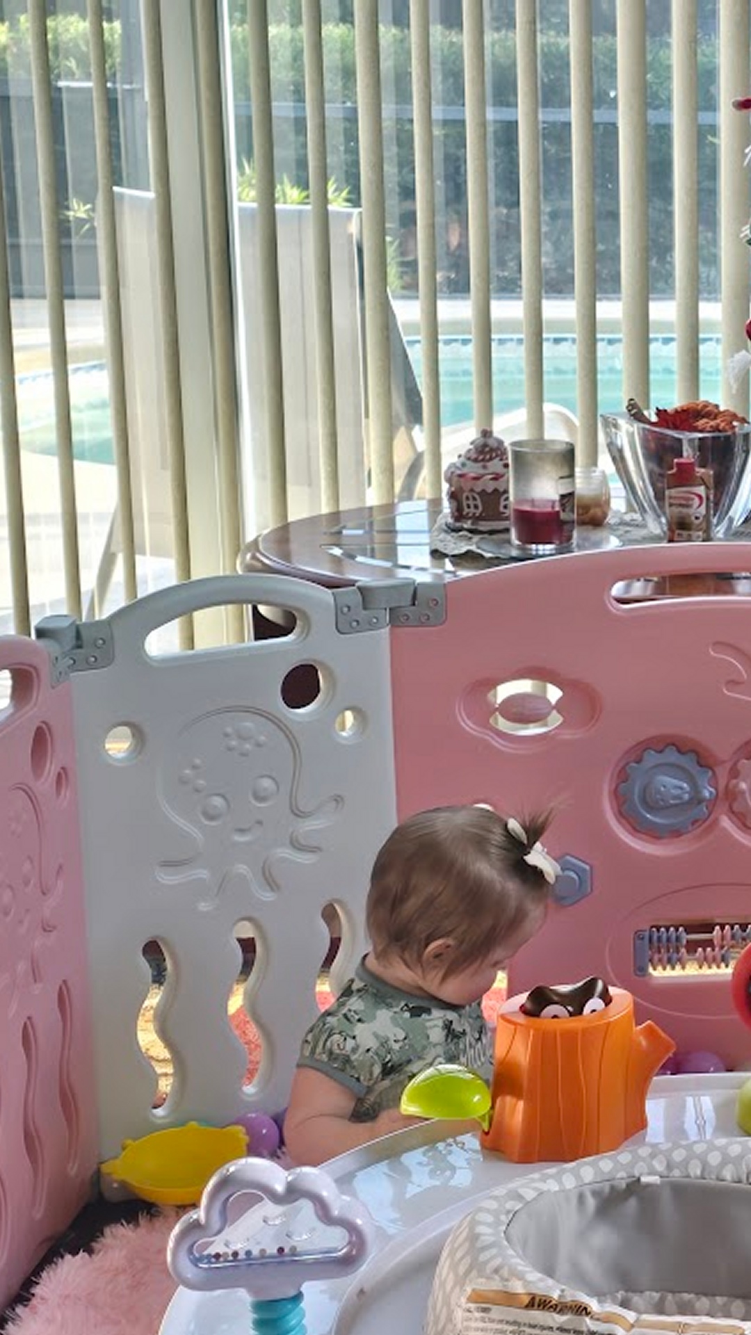 Baby playing inside pink and white playpen with toys in girls room setup for safe play area