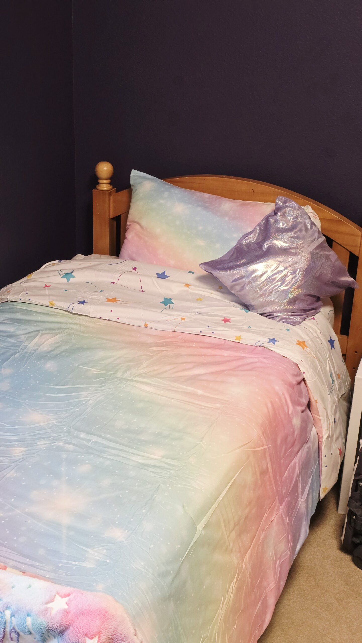 Rainbow girls bedding set on twin bed with colorful galaxy comforter, matching sheets, and glitter accent pillow in girls room makeover