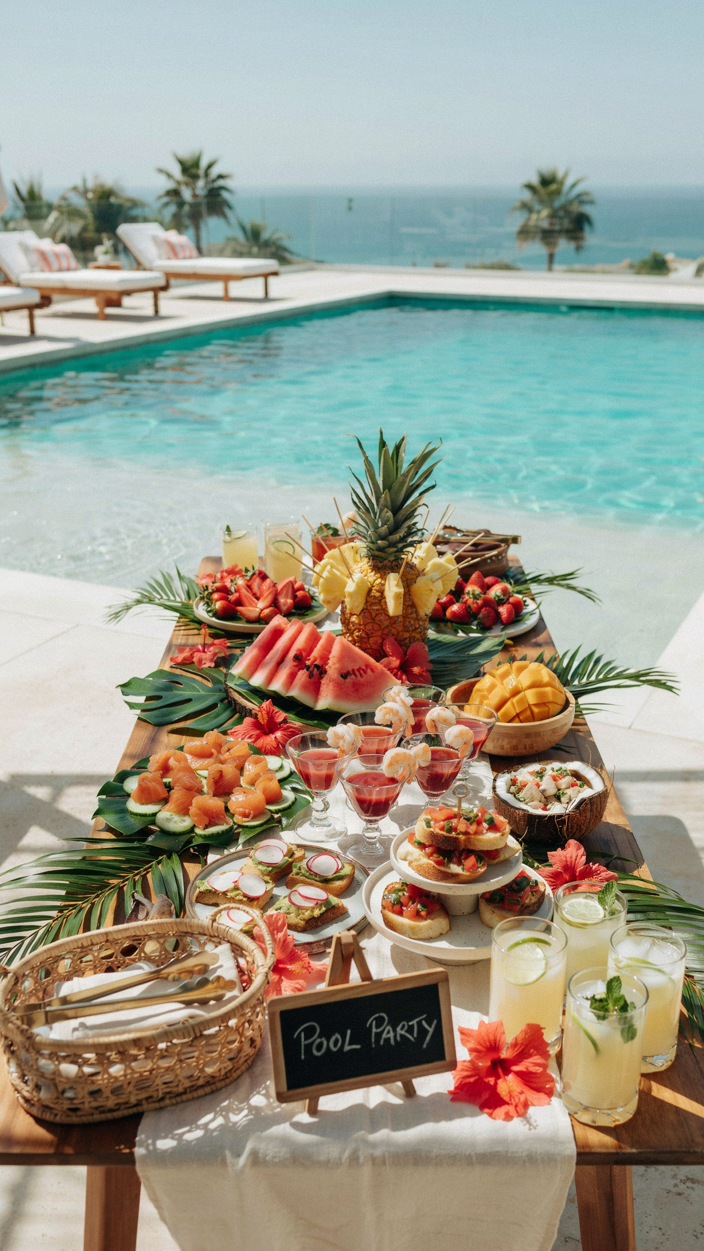 Poolside tropical food display featuring fresh watermelon, pineapple, mango, tropical drinks, seafood appetizers, fruit platters, tropical flowers, and serving trays beside a swimming pool